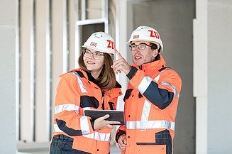 Photo of two people in construction clothing talking on a building site  