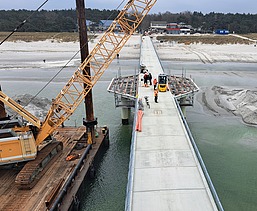 Langer Steg oder Brücke, die von Land ins Meer führt, mit Verbindung zur Baustelle der künstlichen Insel vor Prerow.