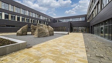 Schulhof des Bertolt-Brech-Schulzentrums mit gelben großen Plastersteinen und dunkelgrauer Fassade in der Mitte sind Natursteine