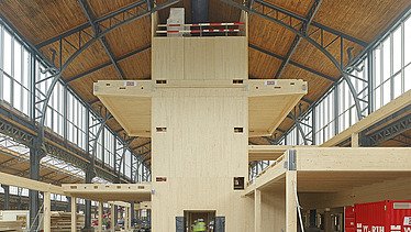 Foto des Hallenraumes des Gare Maritime Brüssel. Riesiger, offener Hallenraum mit Holzdachkonstruktion und Holzgebäude.