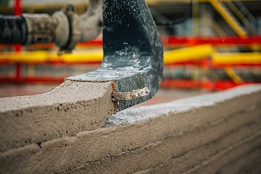 Photo of a print head 3D printing a wall on a construction site