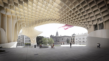 Foto der Marktplatzüberdachung des Metropol Parasol Sevilla. Personen stehen unter einer pilzartigen Holzkonstruktion.