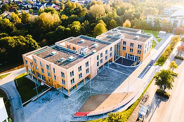 Foto der Uni Witten von außen. Man sieht ein großes Gebäudes aus Holz.