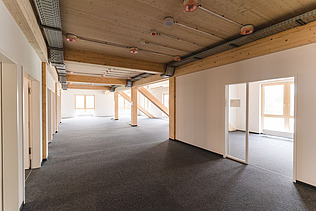 Foto der Uni Witten von innen. Man sieht einen Innenraum mit hellen Wänden und einer Holzdecke