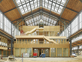 Foto des Hallenraumes des Gare Maritime Brüssel. Riesiger, offener Hallenraum mit Holzdachkonstruktion und Holzgebäude.