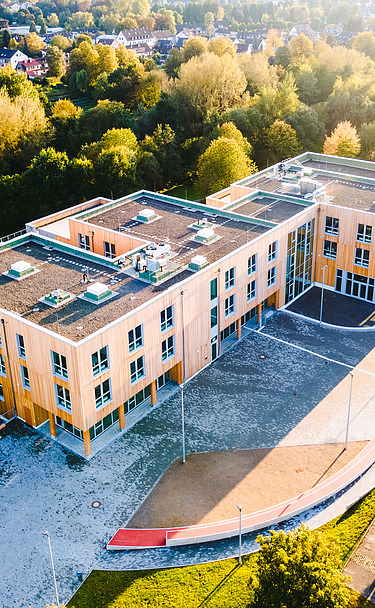 Foto der Uni Witten von außen. Man sieht ein großes Gebäudes aus Holz.