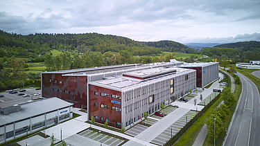 Luftaufnahme eines Gebäudekomplexes aus Holz mit roter Fassadengestaltung.