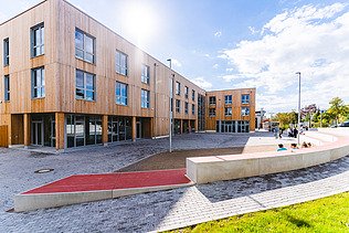 Foto der Uni Witten von außen. Man sieht ein großes Gebäudes aus Holz.