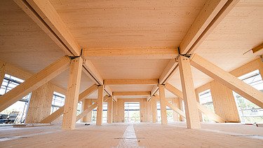 Foto der Uni Witten von innen. Man sieht Brettschichtholzbalken und eine großflächige LENO-Holzdecke.