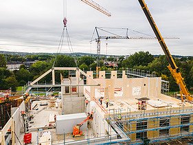 Foto der Uni Witten von außen. Man sieht die Montage großer Holzelemente.