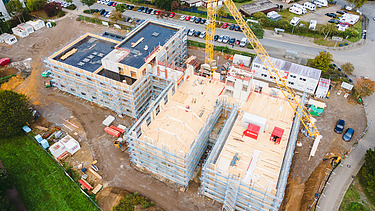 Foto der Uni Witten von außen. Man sieht die Montage großer Holzelemente aus der Vogelperspektive