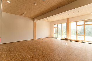 Foto der Uni Witten von innen. Man sieht einen Innenraum mit vielen Holzoberflächen.