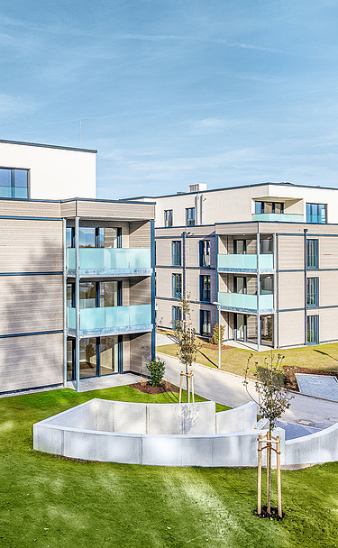 Außenansicht eines der beiden Wohngebäude mit Balkonen und einer Fassade aus Holz und Putz