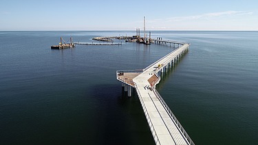 Langer Steg oder Brücke, die von Land ins Meer führt, mit Verbindung zur Baustelle der künstlichen Insel vor Prerow.