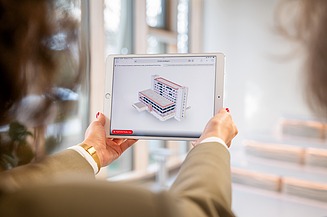 Foto Dame mit Tablet in der Hand, auf dem ein 3D-Modell zu sehen ist