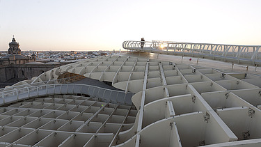 Foto eines Skywalkes des Metropol Parasols in Sevilla Spanien. Man sieht eine Person in der Abenddämmerung  auf dem Skywalk stehen.