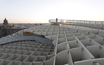 Foto eines Skywalkes des Metropol Parasols in Sevilla Spanien. Man sieht eine Person in der Abenddämmerung  auf dem Skywalk stehen.