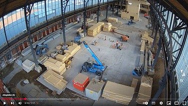 Foto eines Hallenraumes im Gare Maritime in Brüssel. Zu sehen sind viele Holzstapel und Fahrzeuge.