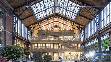 Foto des Hallenraumes des Gare Maritime Brüssel. Riesiger, offener Hallenraum mit Holzdachkonstruktion.