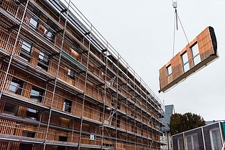 Foto des Collegium Academicums in Heidelberg während der Montage. Man sieh ein LENO-Holzelement schwebend am Kran.