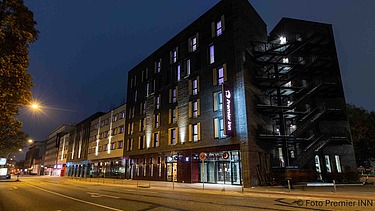 Nachtansicht des Hotels PREMIER INN Hamburg-St. Pauli mit beleuchteter Fassade