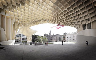 Foto der Marktplatzüberdachung des Metropol Parasol Sevilla. Personen stehen unter einer pilzartigen Holzkonstruktion.