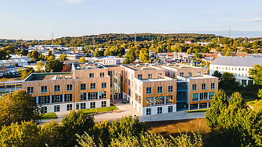 Foto der Uni Witten von außen. Man sieht ein großes Gebäudes aus Holz.