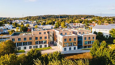 Foto der Uni Witten von außen. Man sieht ein großes Gebäudes aus Holz.