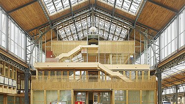 Foto des Hallenraumes des Gare Maritime Brüssel. Riesiger, offener Hallenraum mit Holzdachkonstruktion und Holzgebäude.