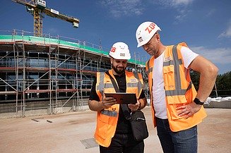 Photo of two employees on a construction site looking at digital plans on a tablet      