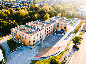 Foto der Uni Witten von außen. Man sieht ein großes Gebäudes aus Holz aus der Vogelperspektive.