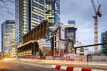 Picture at night of a high-rise building, a crane in the background and construction site objects in the foreground