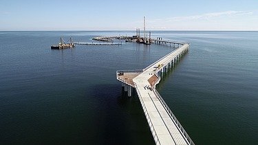 Langer Steg oder Brücke, die von Land ins Meer führt, mit Verbindung zur Baustelle der künstlichen Insel vor Prerow.