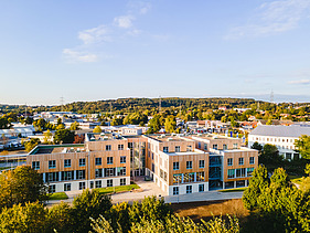 Foto der Uni Witten von außen. Man sieht ein großes Gebäudes aus Holz.