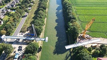 Drohnenaufnahme (Top-View) der Baustelle Hertha-Peters-Brücke, ein Kran hebt die Stahlkonstruktion