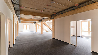 Foto der Uni Witten von innen. Man sieht einen Innenraum mit hellen Wänden und einer Holzdecke