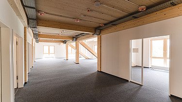 Foto der Uni Witten von innen. Man sieht einen Innenraum mit hellen Wänden und einer Holzdecke