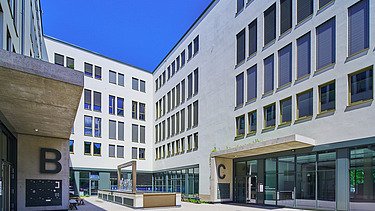 Innenhof des S-förmigen Gebäude mit Brunnenelement und begrünten Vordächern