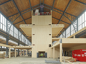 Foto des Hallenraumes des Gare Maritime Brüssel. Riesiger, offener Hallenraum mit Holzdachkonstruktion und Holzgebäude.