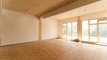 Foto der Uni Witten von innen. Man sieht einen Innenraum mit vielen Holzoberflächen.