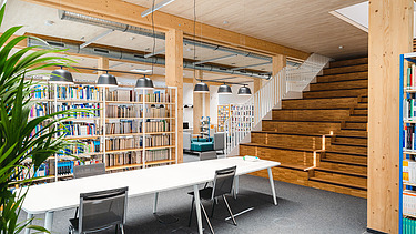 Foto der Bibliothek der Uni Witten. Man sieht viele Bücher, eine Holzdecke und Holztreppe.