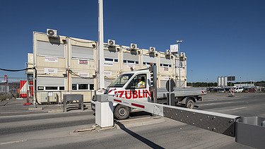 Bild von einer Zufahrtskontrolle, ein Auto fährt durch und Baucontainern im Hintergrund