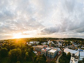 Foto der Uni Witten von außen. Man sieht den Rohbau aus Holz in der Vogelperspektive in dämmriger Lichtstimmung.