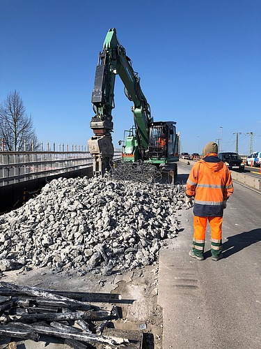 Photo of a person and an excavator with a pile of rubble