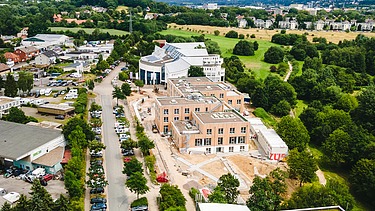 Foto der Uni Witten von außen. Man sieht ein großes Gebäudes aus Holz aus der Vogelperspektive.