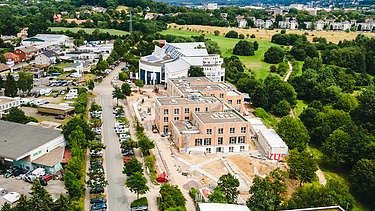 Foto der Uni Witten von außen. Man sieht ein großes Gebäudes aus Holz aus der Vogelperspektive.