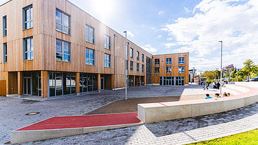 Foto der Uni Witten von außen. Man sieht ein großes Gebäudes aus Holz.