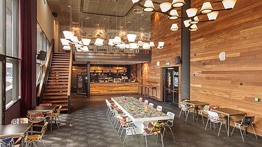 Im Holzstil gestaltete Cafetria mit vielen weißen Hängeleuchten und einer Treppe