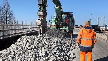 Photo of a person and an excavator with a pile of rubble