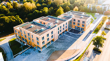 Foto der Uni Witten von außen. Man sieht ein großes Gebäudes aus Holz aus der Vogelperspektive.